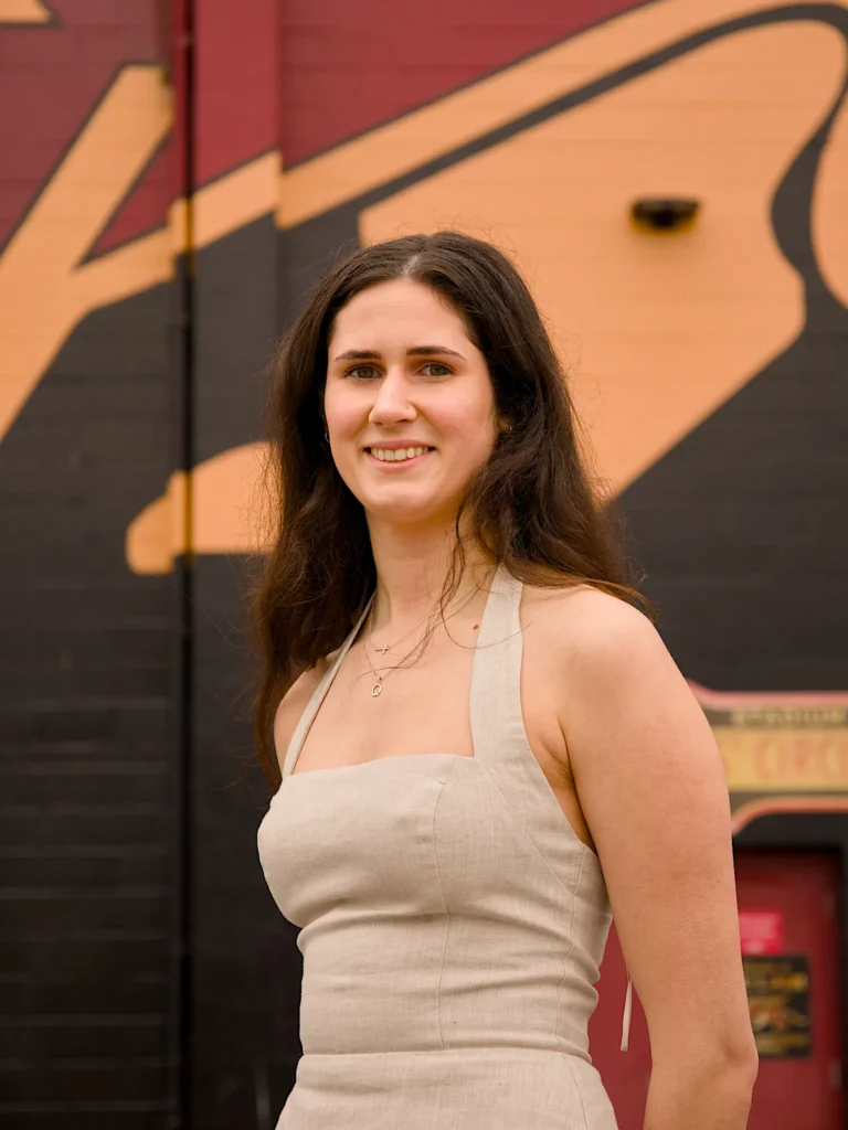 A University of Guelph graduate in regalia pictured close up against the campus mural wall.